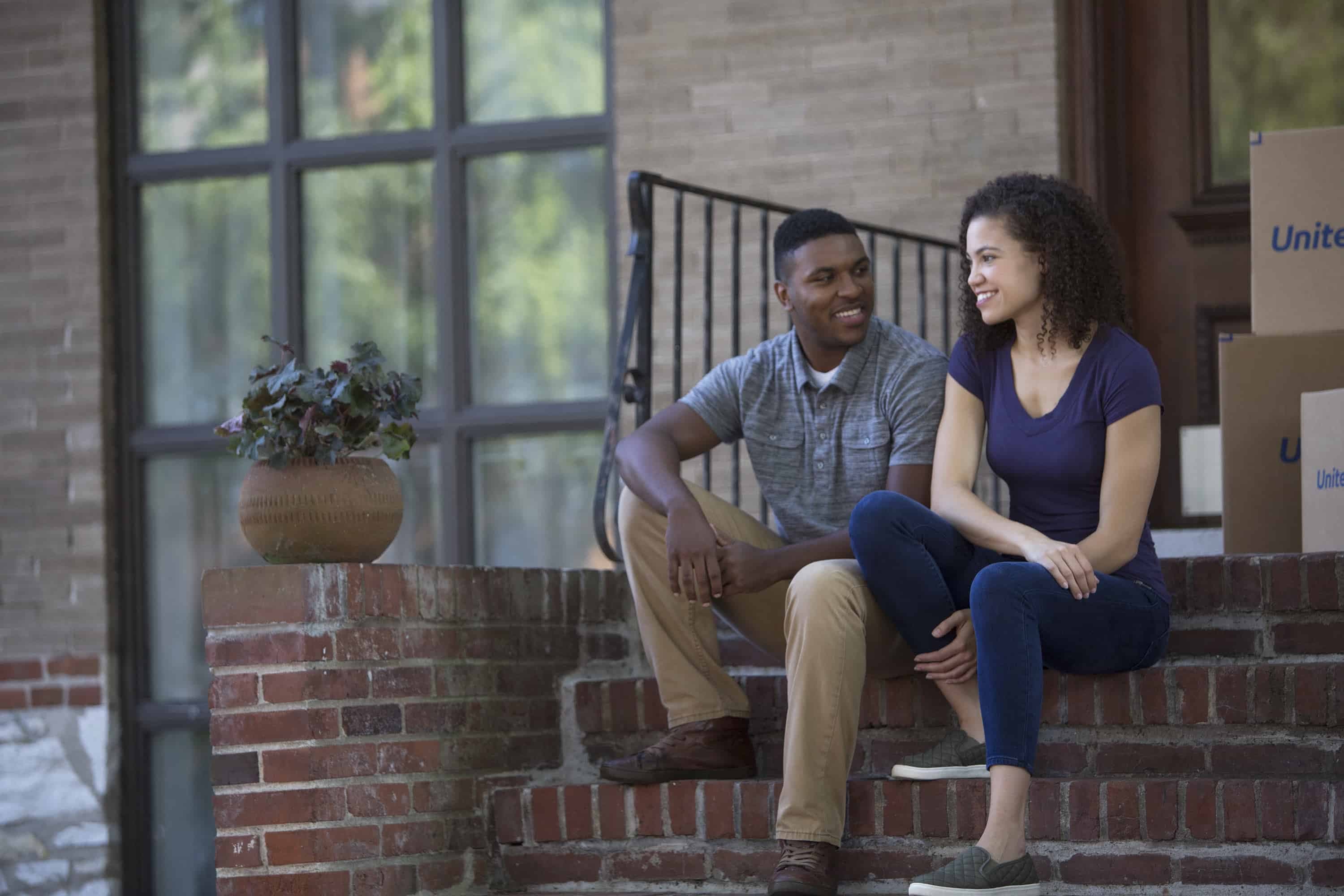 young couple sitting outside of their condo on the stairs with moving boxes beside them - United Van Lines®