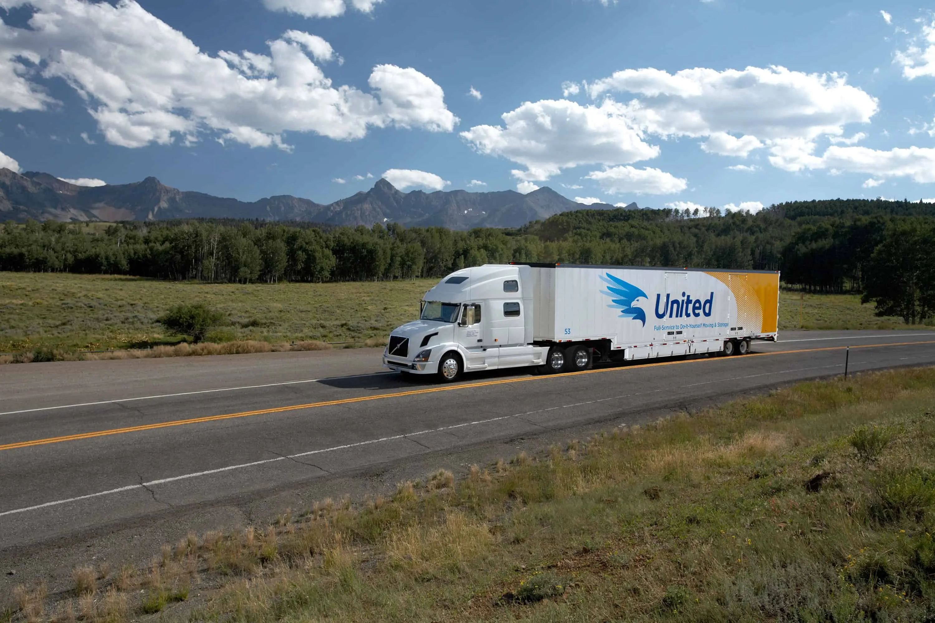 Car Shipping - Unted truck driving on a rural highway with trees and mountains in the distance - United Van Lines