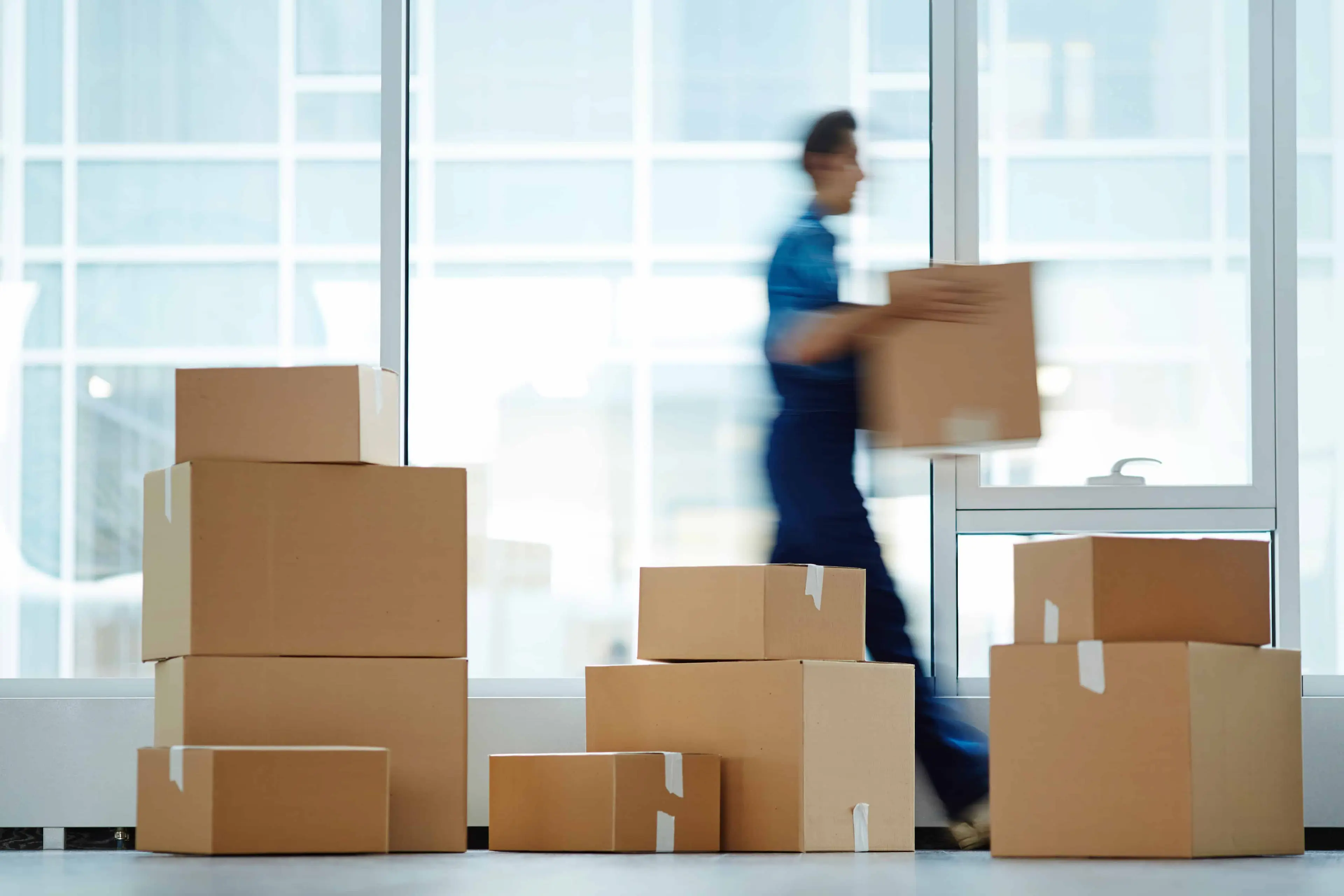 How to Avoid Moving Scams - stacks of moving boxes with a mover in the background - United Van Lines