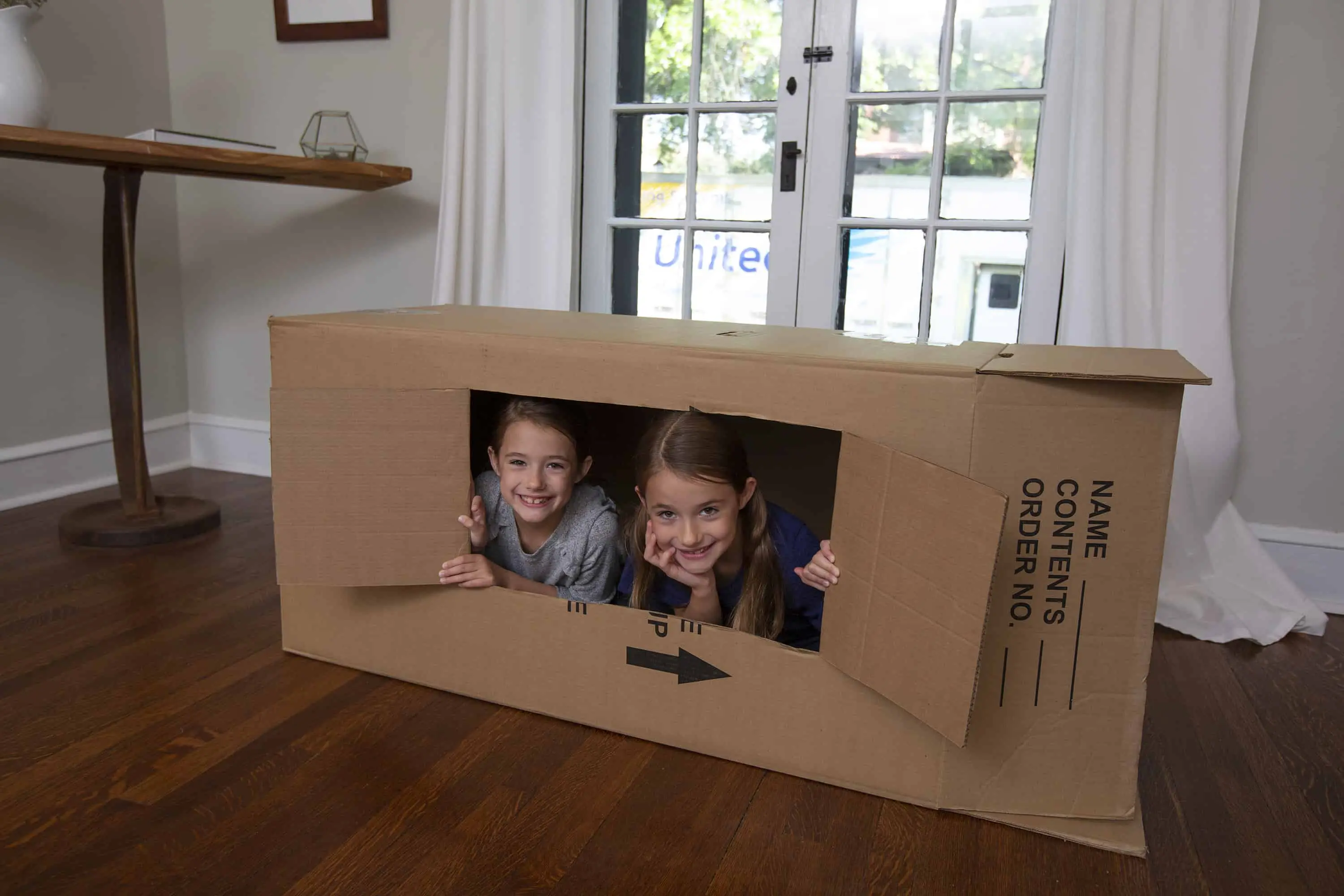 two young twin girls in a box made into a fort- United Van Lines